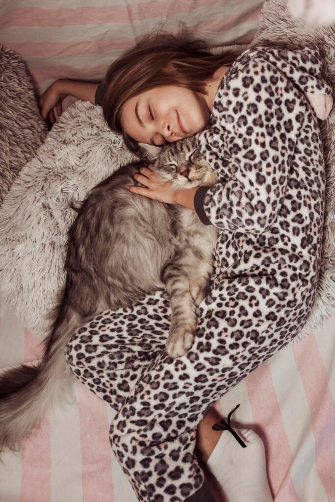 girl pajamas hugging her cat laying bed - Fenomena kucing jilat karpet: Apakah ini normal?